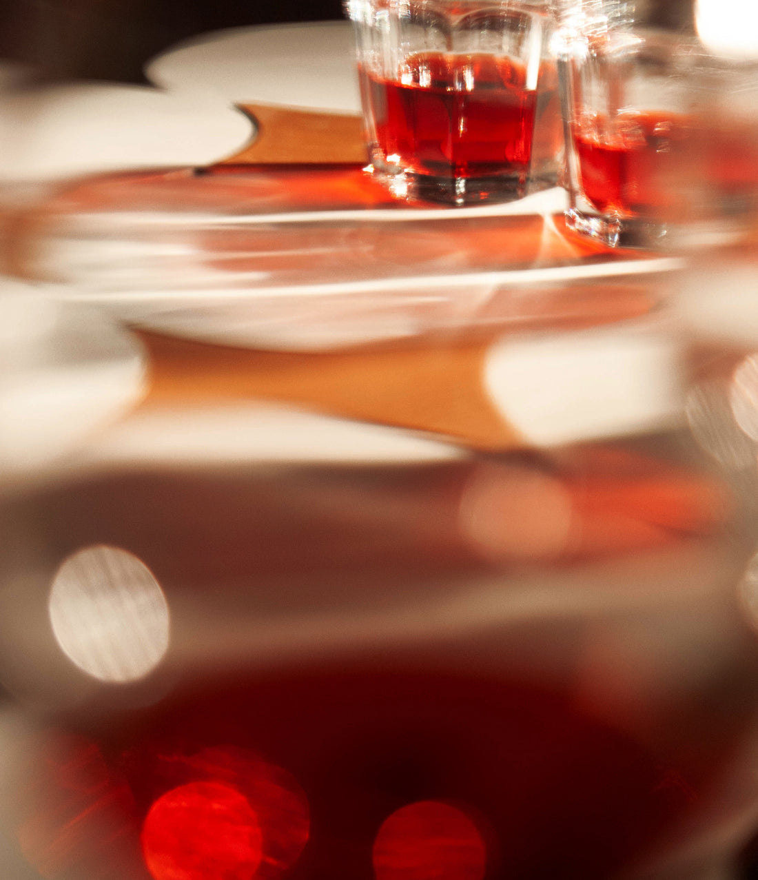 Two glasses of red liquid on a table with blurred lights in the foreground