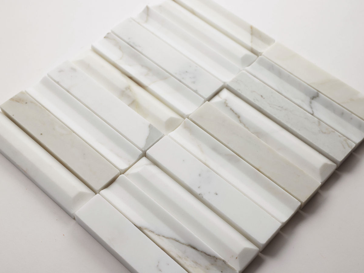 A close-up of white marble tiles with gray veining, arranged in a grid pattern with raised, grooved textures.