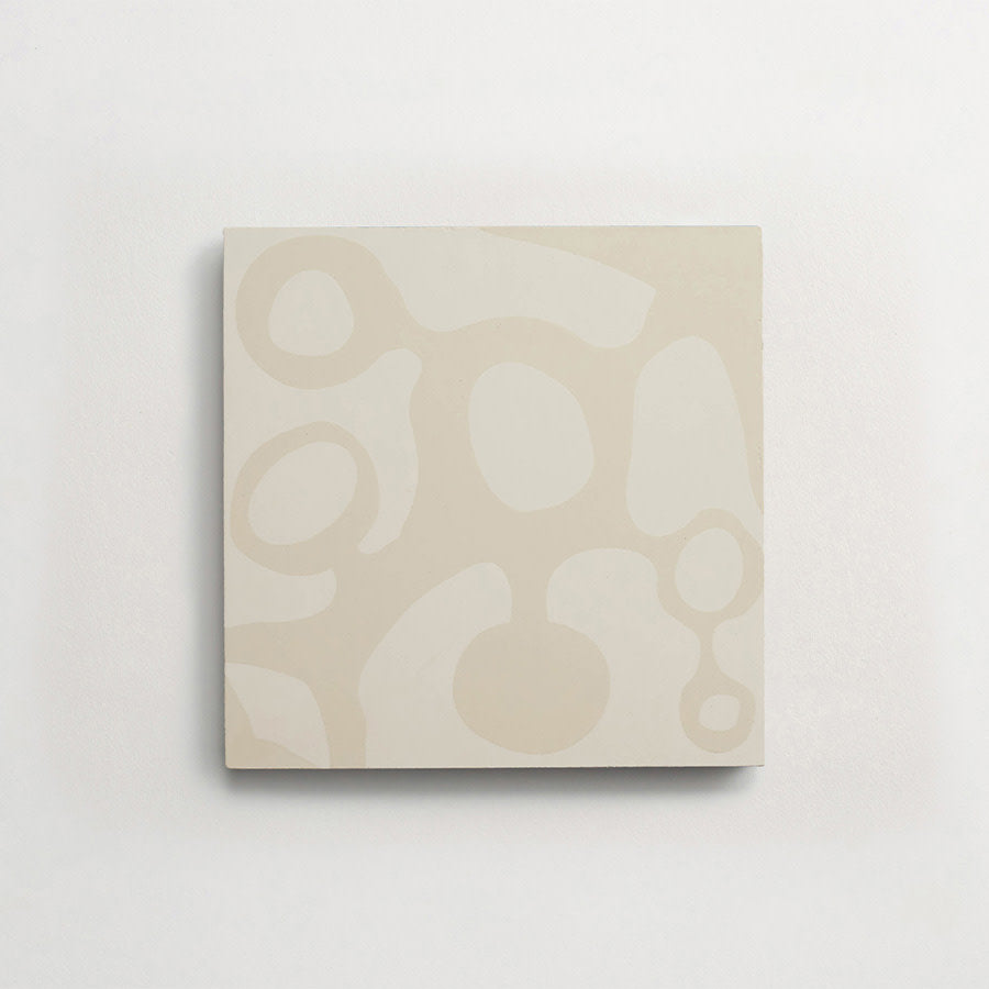 A square tile with an abstract pattern of light beige organic shapes on a white background, mounted on a plain white wall.