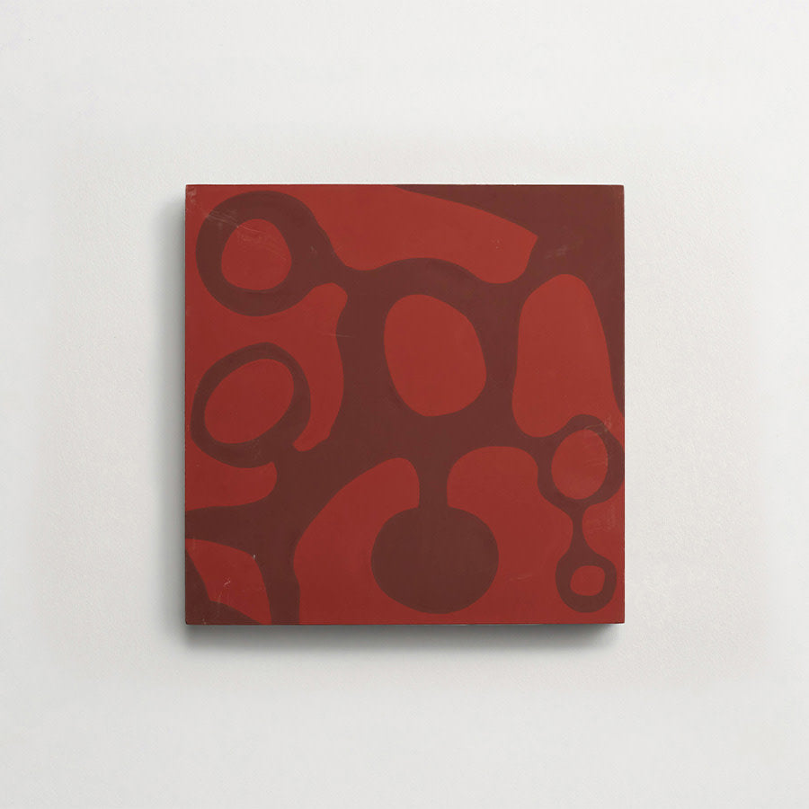 A square canvas with abstract dark red organic shapes on a lighter red background, mounted on a white wall.