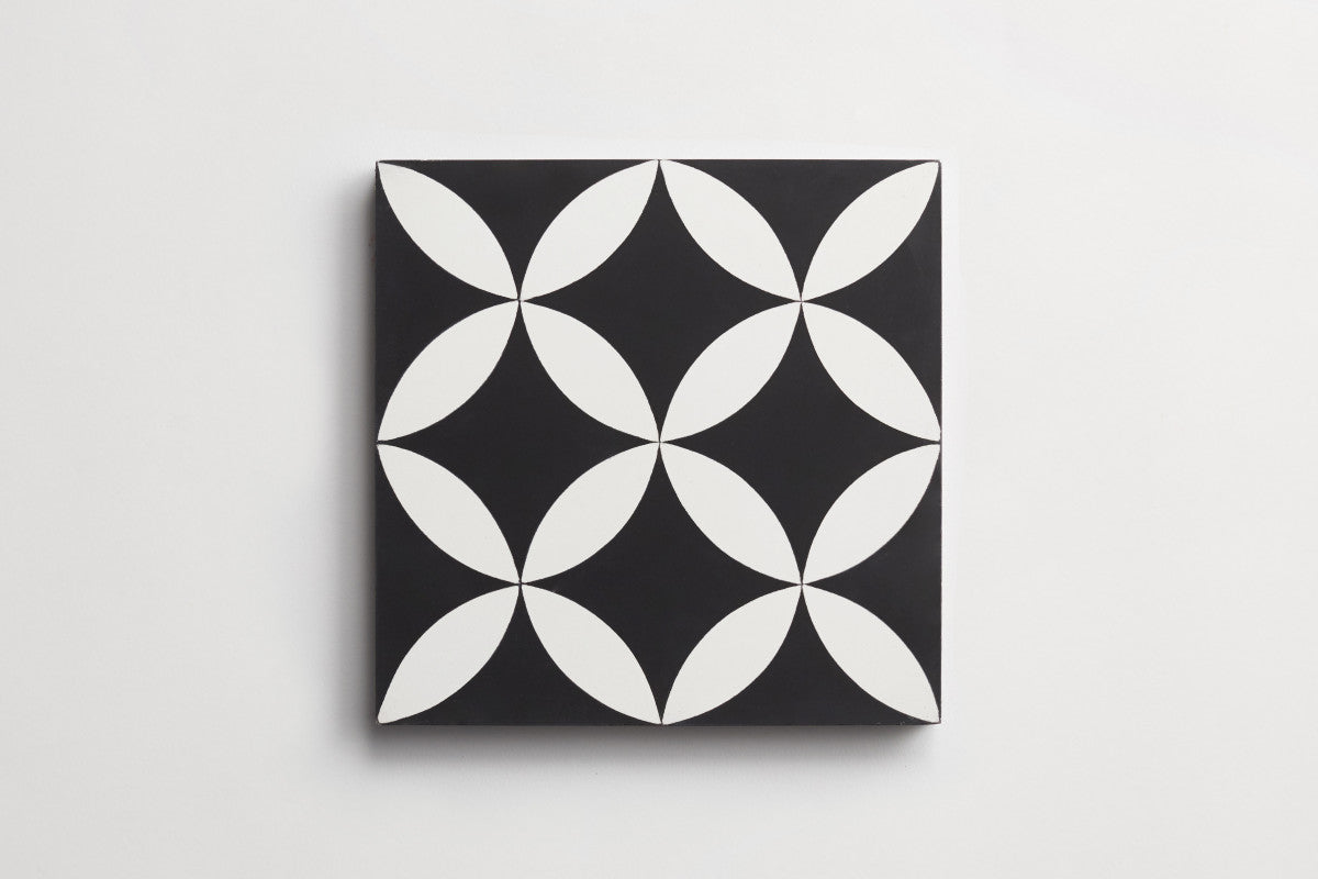 A square tile with a black background featuring a repeating white geometric pattern of intersecting ovals forming a circular motif.