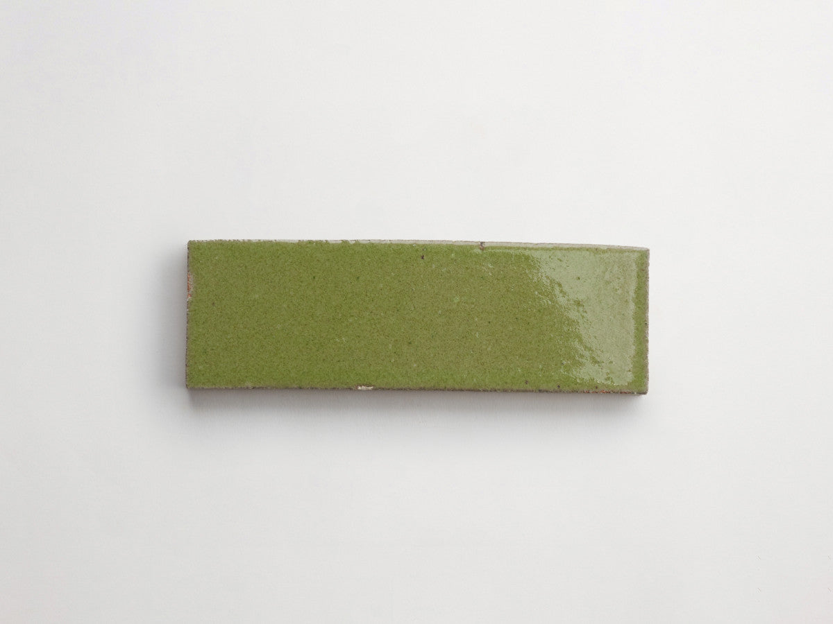 A rectangular, glossy green ceramic tile is placed on a plain white background.