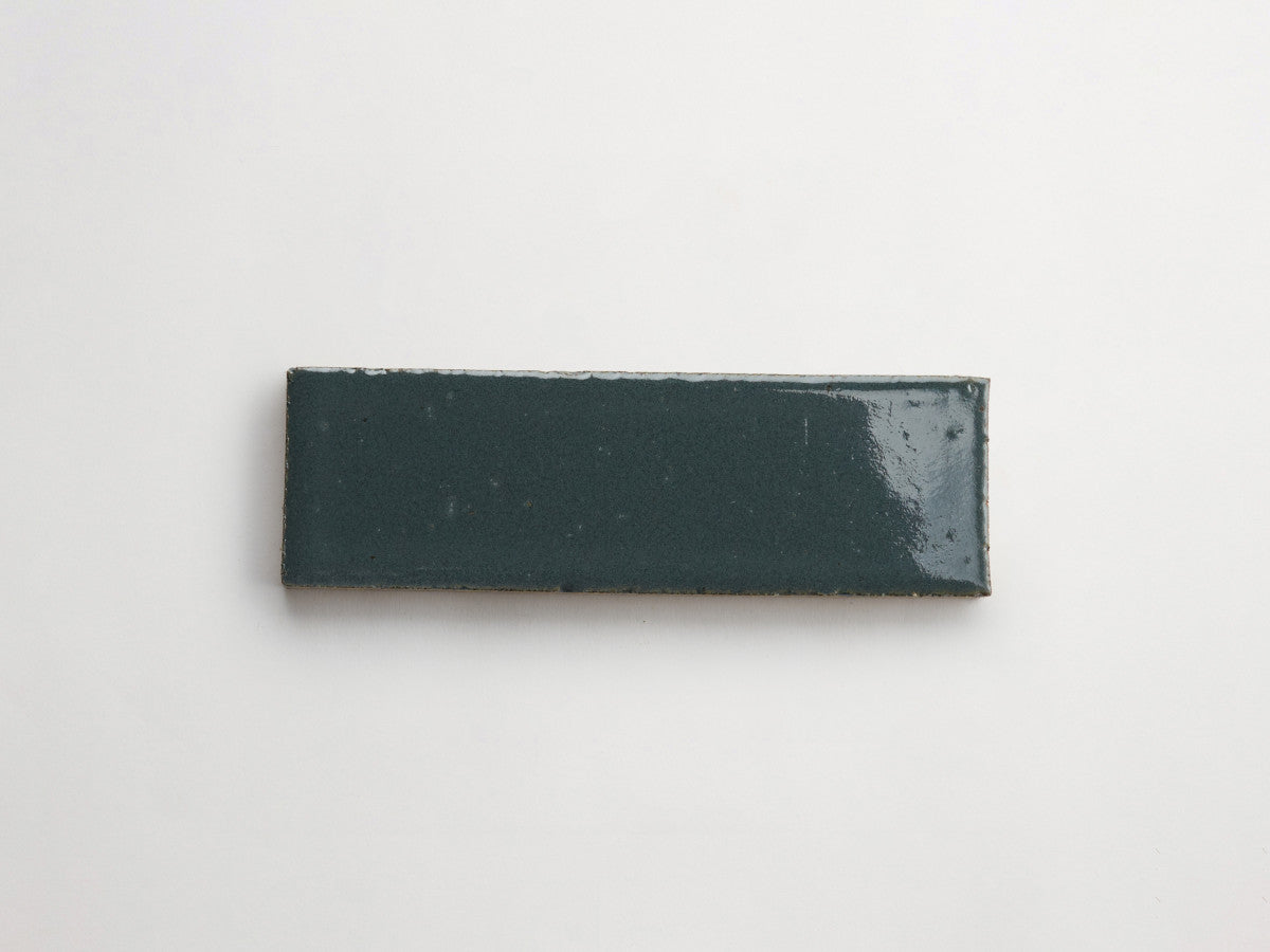 A rectangular, glossy dark green ceramic tile is placed on a plain white background.