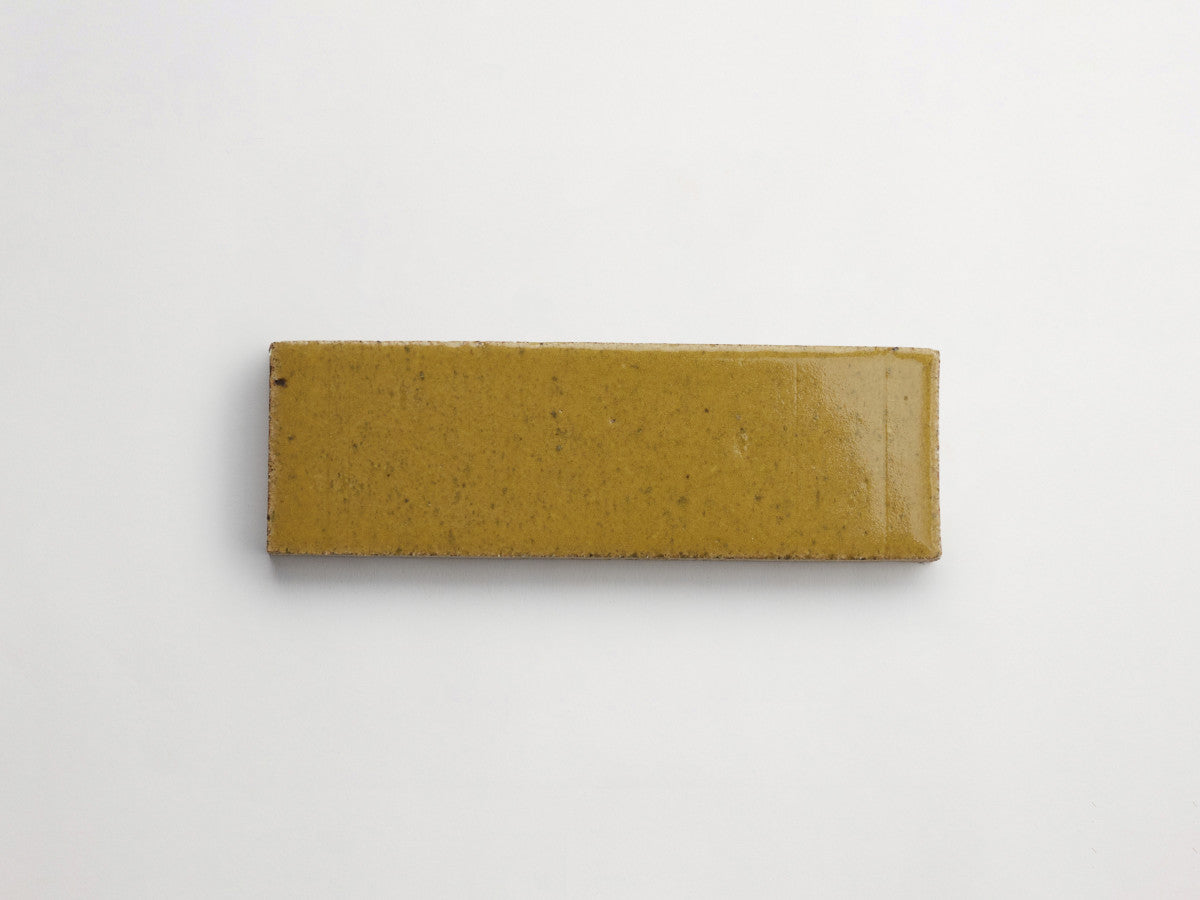 A rectangular, yellowish-brown ceramic tile placed on a plain white background.