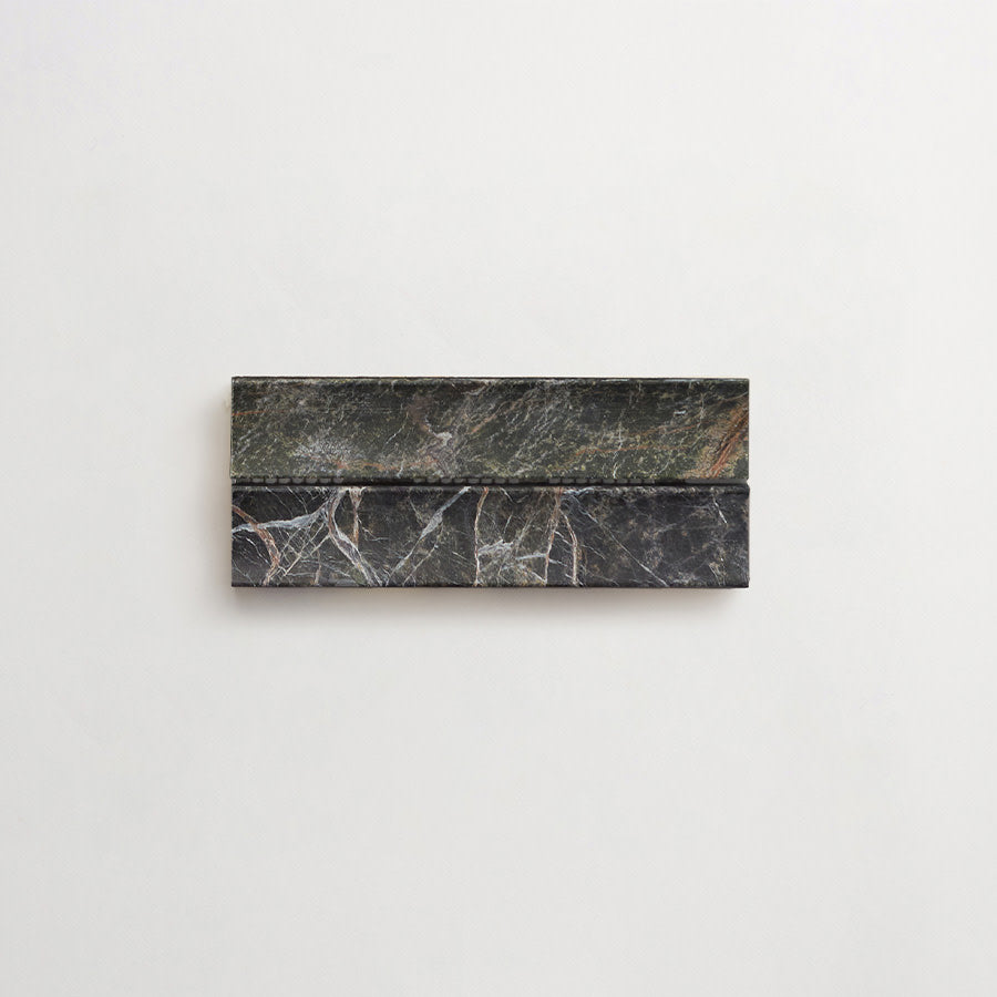 A rectangular object made of dark, veined marble is mounted horizontally on a plain white wall.