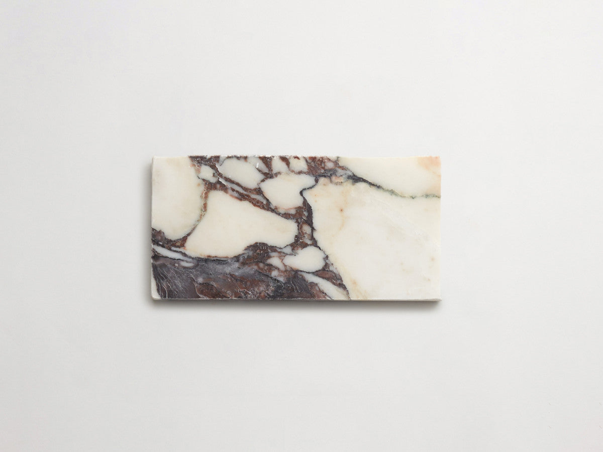 A rectangular piece of marble features a white base with dark brown and beige veining, placed on a plain white background.