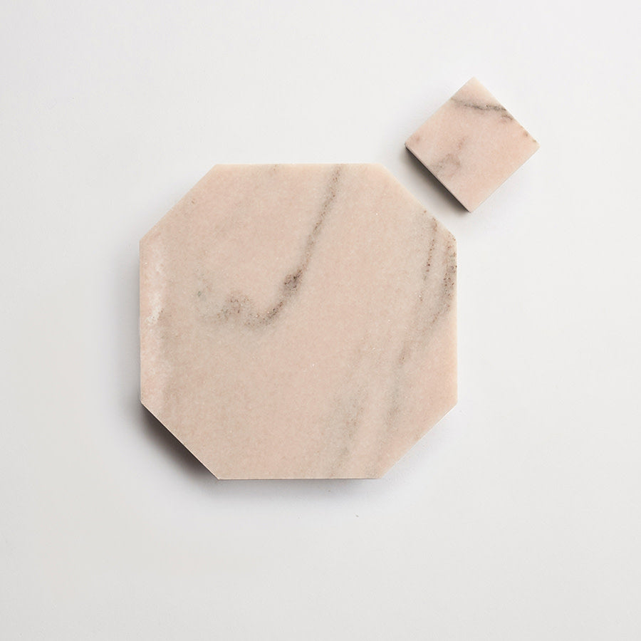 A large octagonal slab and a small square tile, both made of light pink marble with subtle gray veining, are placed on a white background.