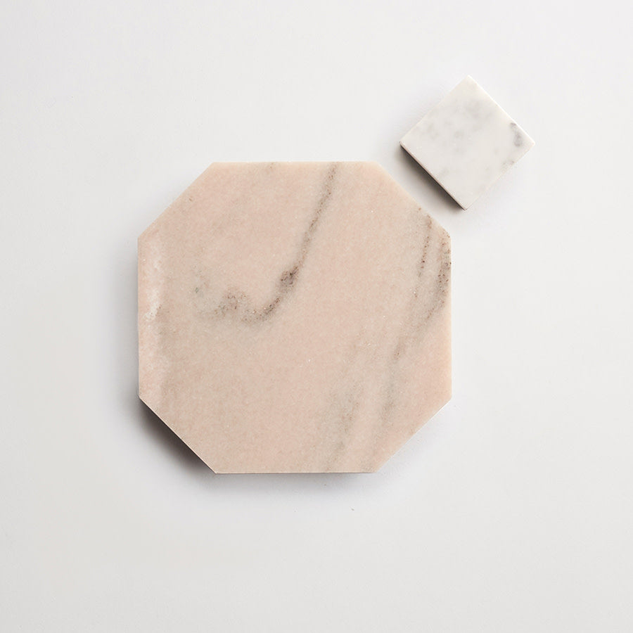 A large, octagonal beige marble tile with faint veining is placed next to a smaller, square white marble tile on a white background.