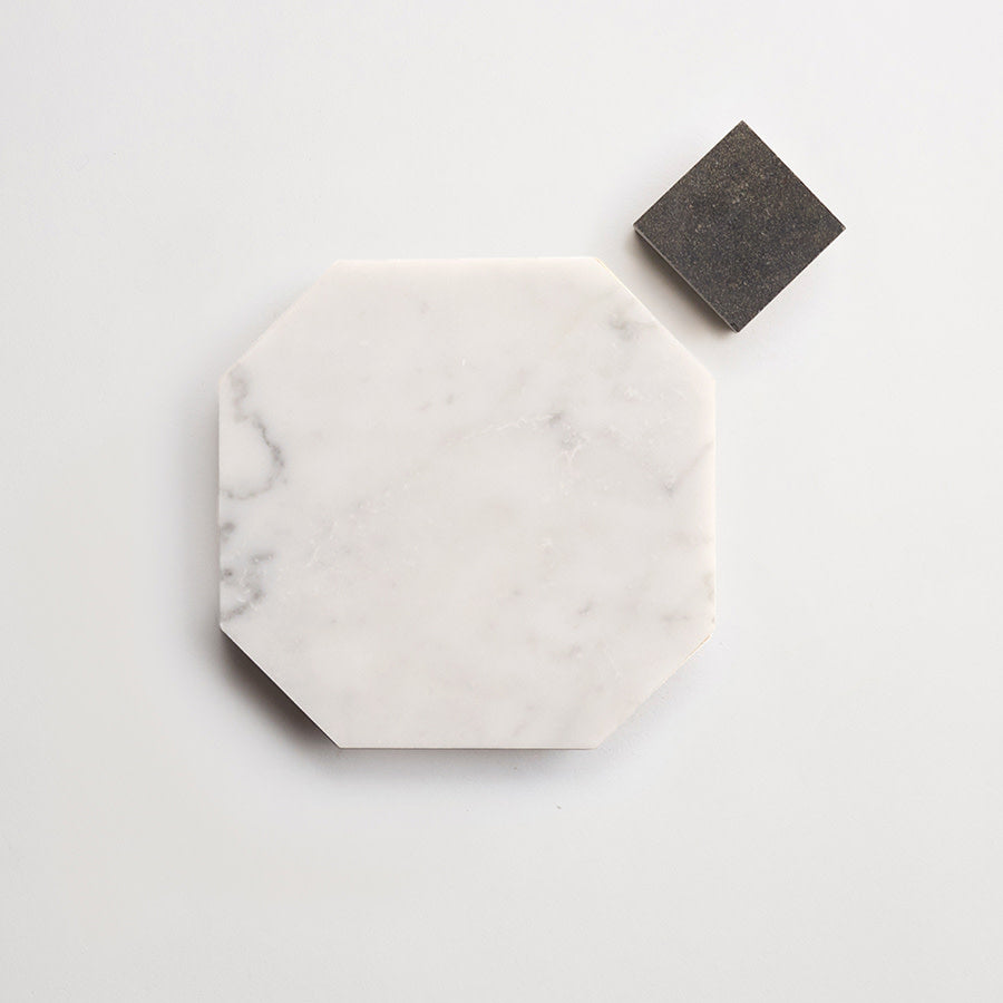 A white octagonal marble tile and a smaller dark gray square tile are placed on a plain light background.