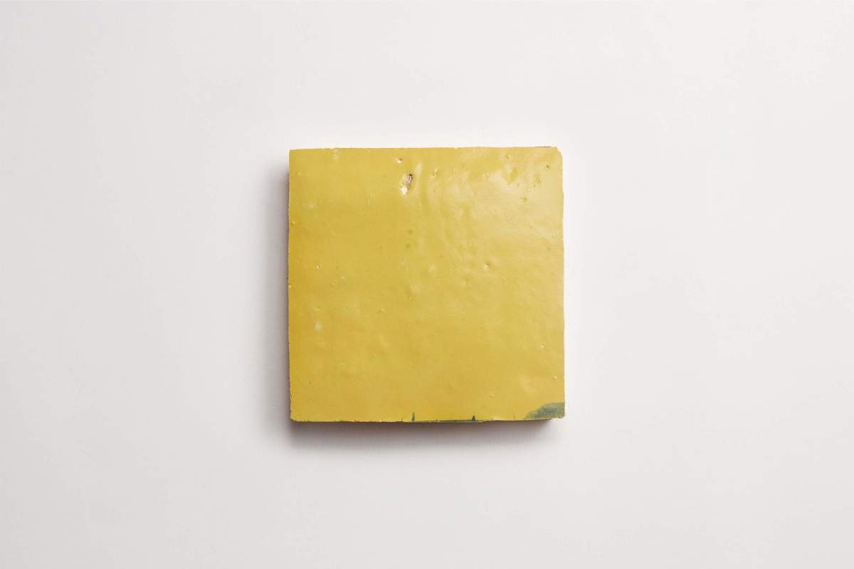 A single square yellow tile with a slightly uneven surface, placed on a plain white background.