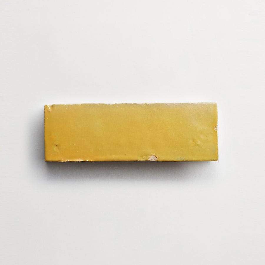 A rectangular yellow ceramic tile with a glossy finish and small chips on the edges, placed on a plain white background.
