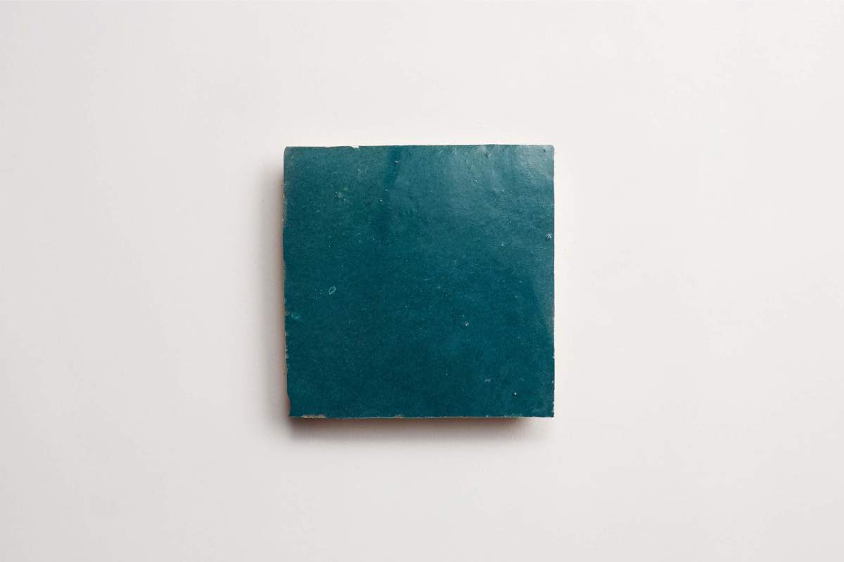 A single square teal ceramic tile is placed on a plain white background.