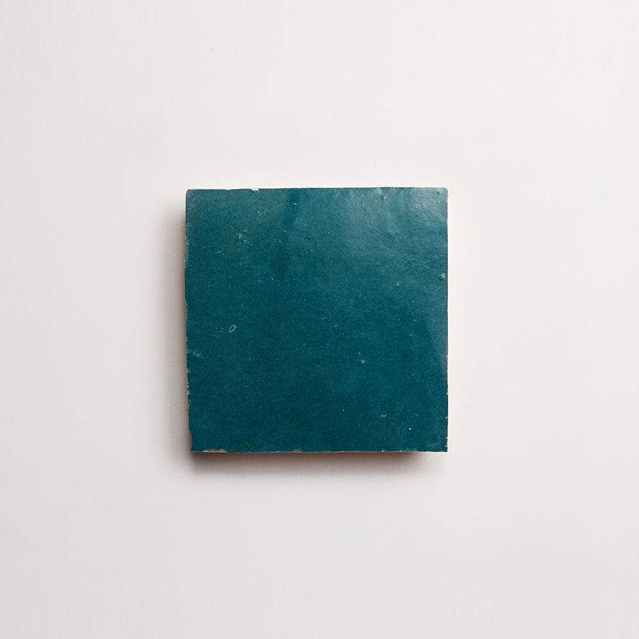 A single square teal ceramic tile placed on a plain white background.