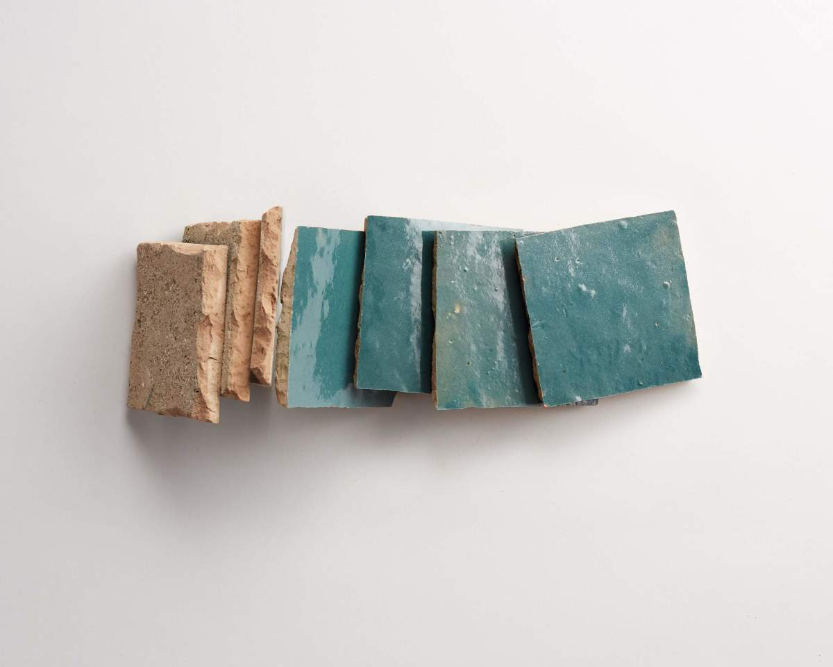 Several broken terracotta tiles are lined up next to several broken teal glazed tiles on a white background.