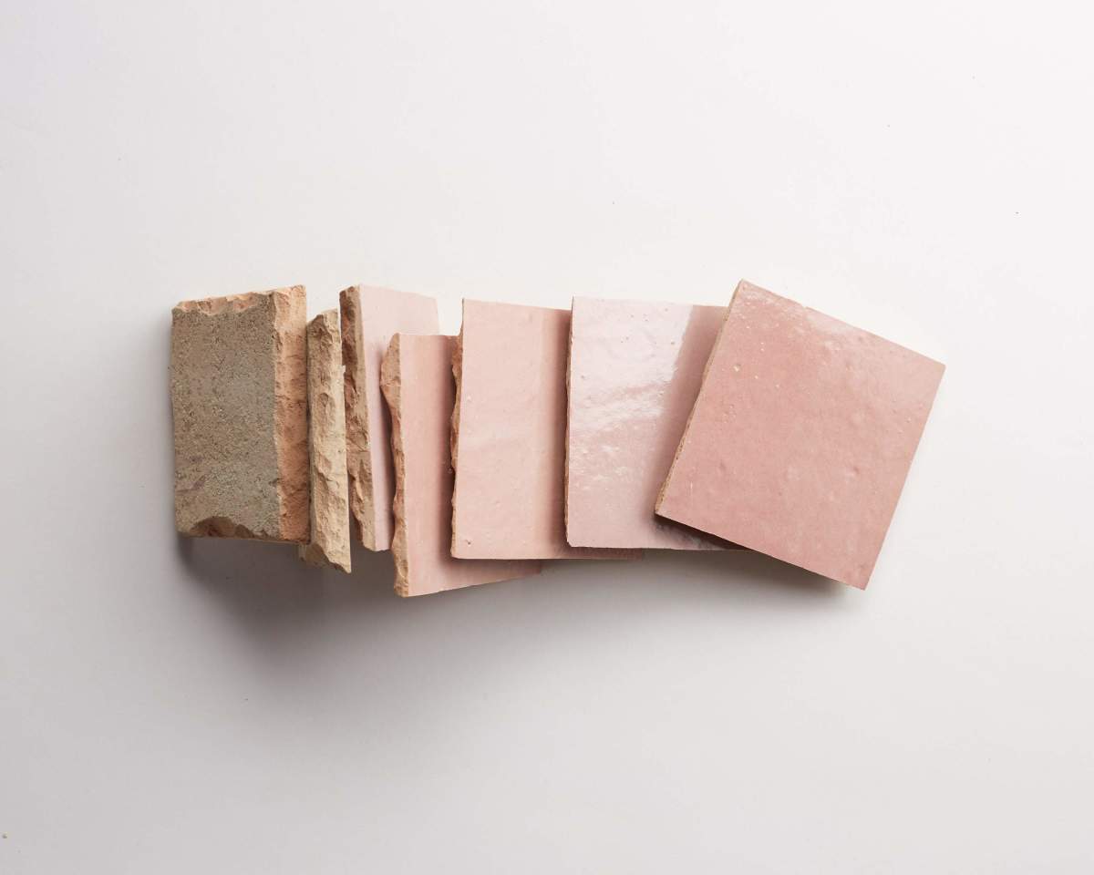 Seven pink ceramic tiles are arranged in a slightly overlapping row on a white background, with some tiles showing their rough, unfinished edges.