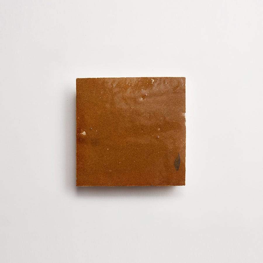 A single square piece of brown jaggery placed on a plain white background.