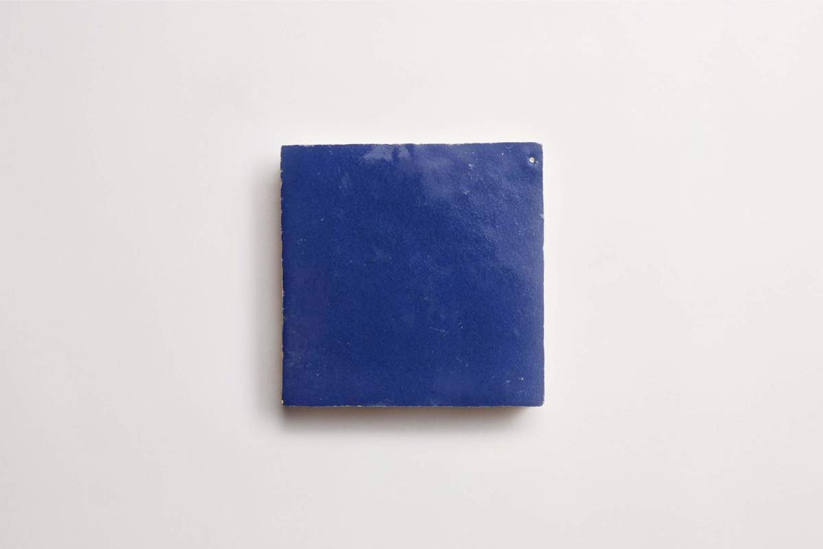 A single square blue tile with a smooth, glossy surface sits centered on a plain white background.