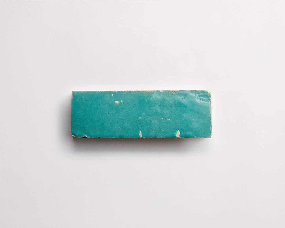 A rectangular turquoise ceramic tile with a glossy finish and small chips along the edges, displayed on a white background.