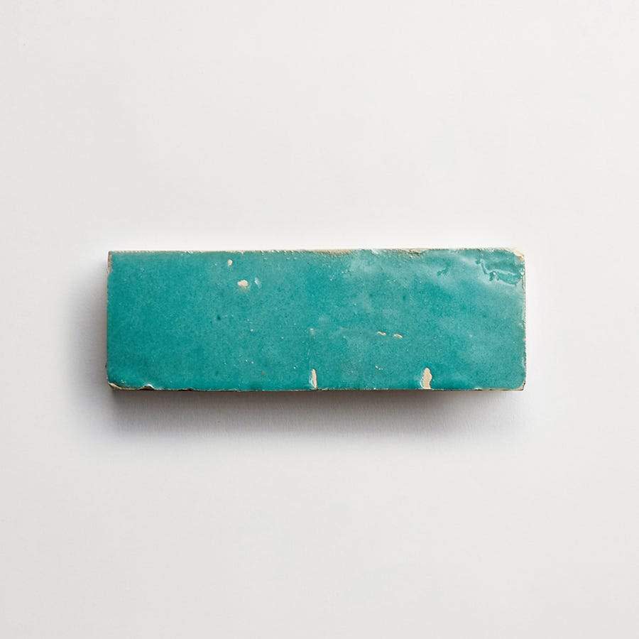 A rectangular turquoise ceramic tile with worn edges and small chips, displayed on a plain white background.