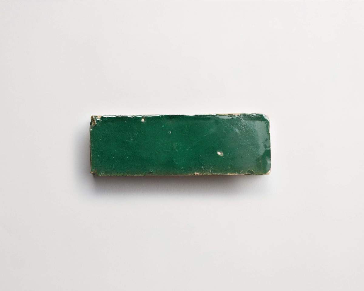 A rectangular green ceramic tile with slightly worn edges on a plain white background.