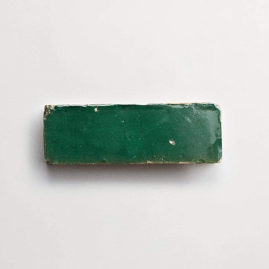 A rectangular green ceramic tile with a glossy finish and slightly worn edges, placed on a plain white background.