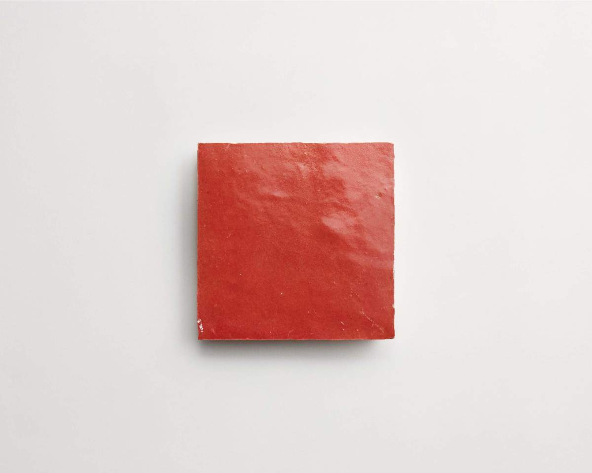 A single red square tile with a glossy surface is placed on a plain white background.