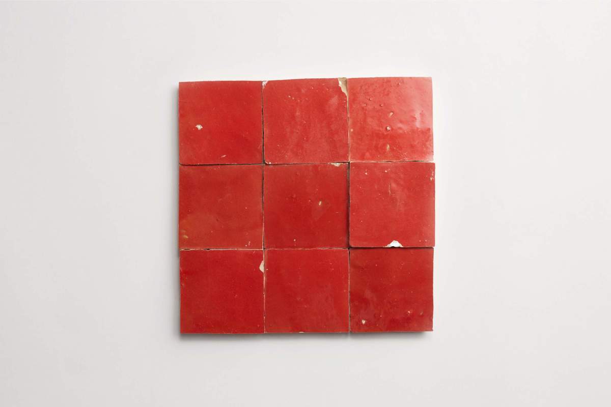Nine red ceramic tiles are arranged in a 3x3 grid on a white background, with slight imperfections and chips visible on some tiles.