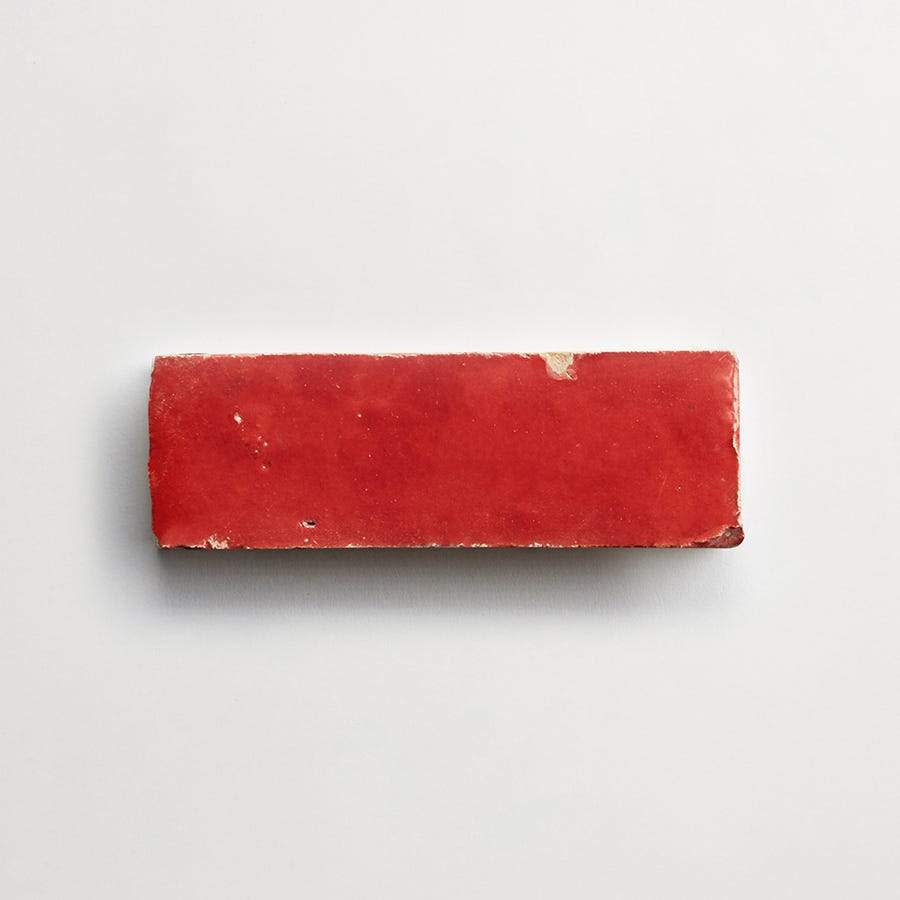 A rectangular red brick with a glossy finish and slightly chipped edges, placed on a plain white background.