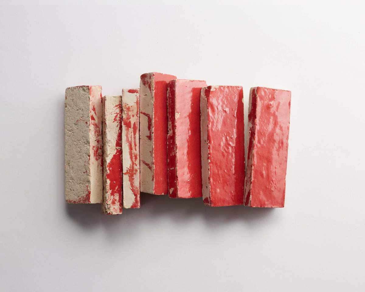 Six rectangular clay bricks with chipped red paint are arranged in a row on a white background.