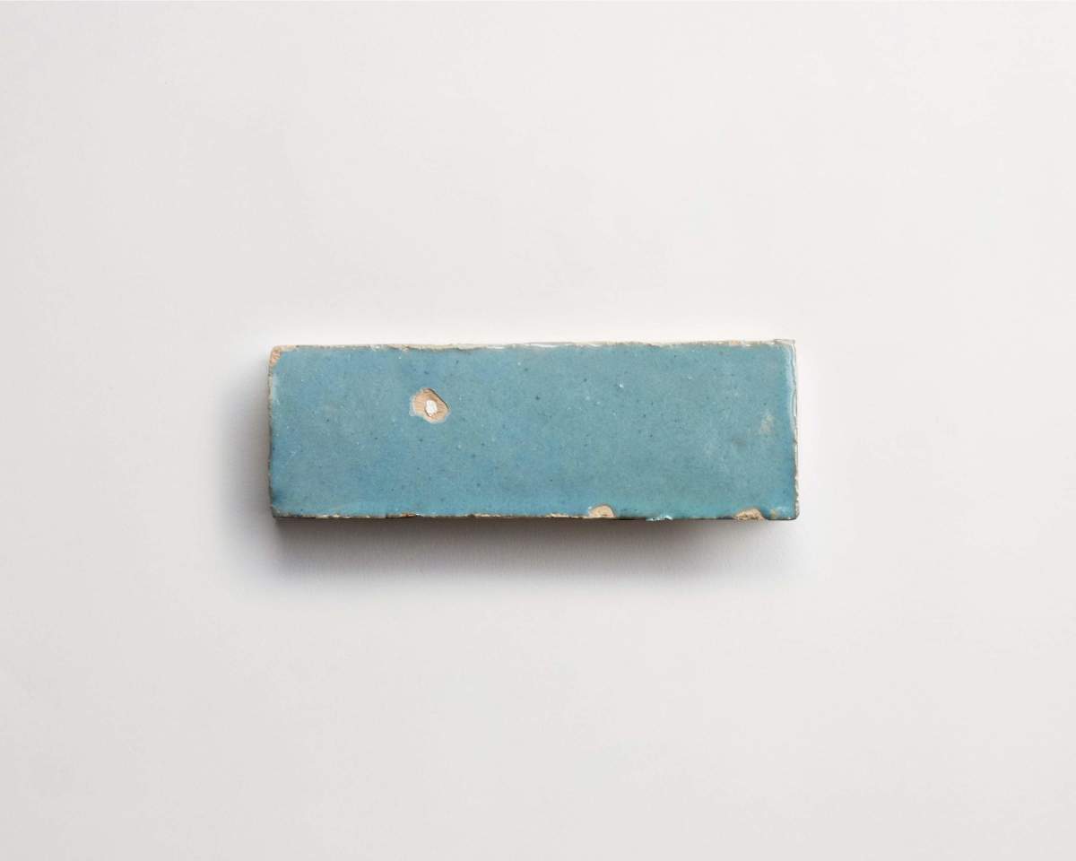 A rectangular blue ceramic tile with chipped edges and small imperfections, placed on a plain white background.