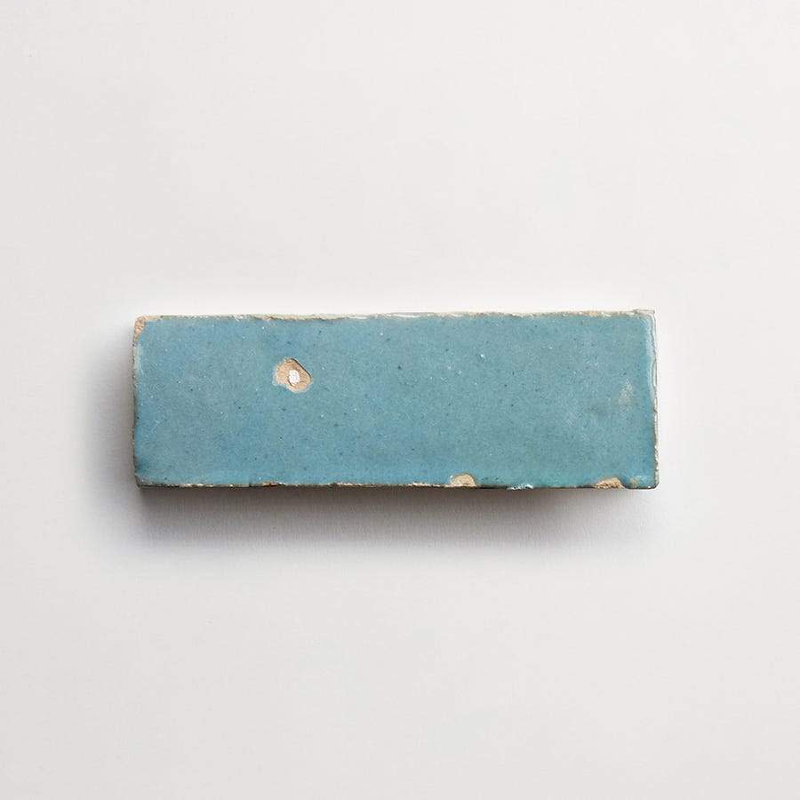 A rectangular blue ceramic tile with slightly rough edges and minor chips, placed on a plain white background.