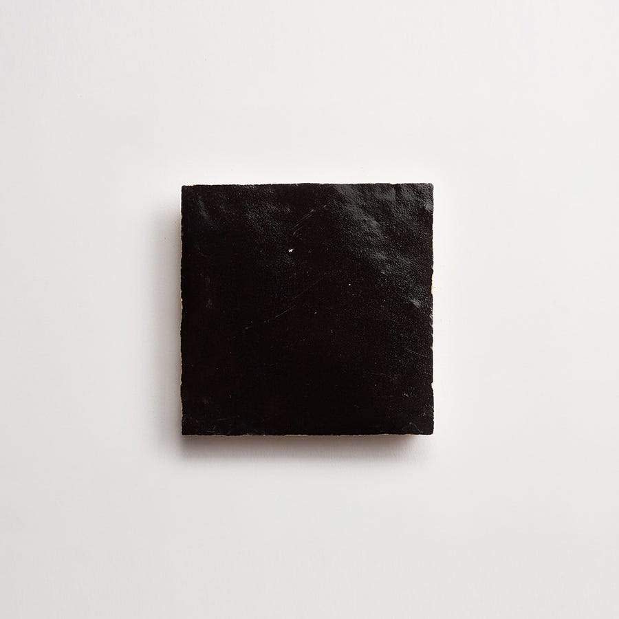 A single, square-shaped piece of black licorice placed on a plain white background.