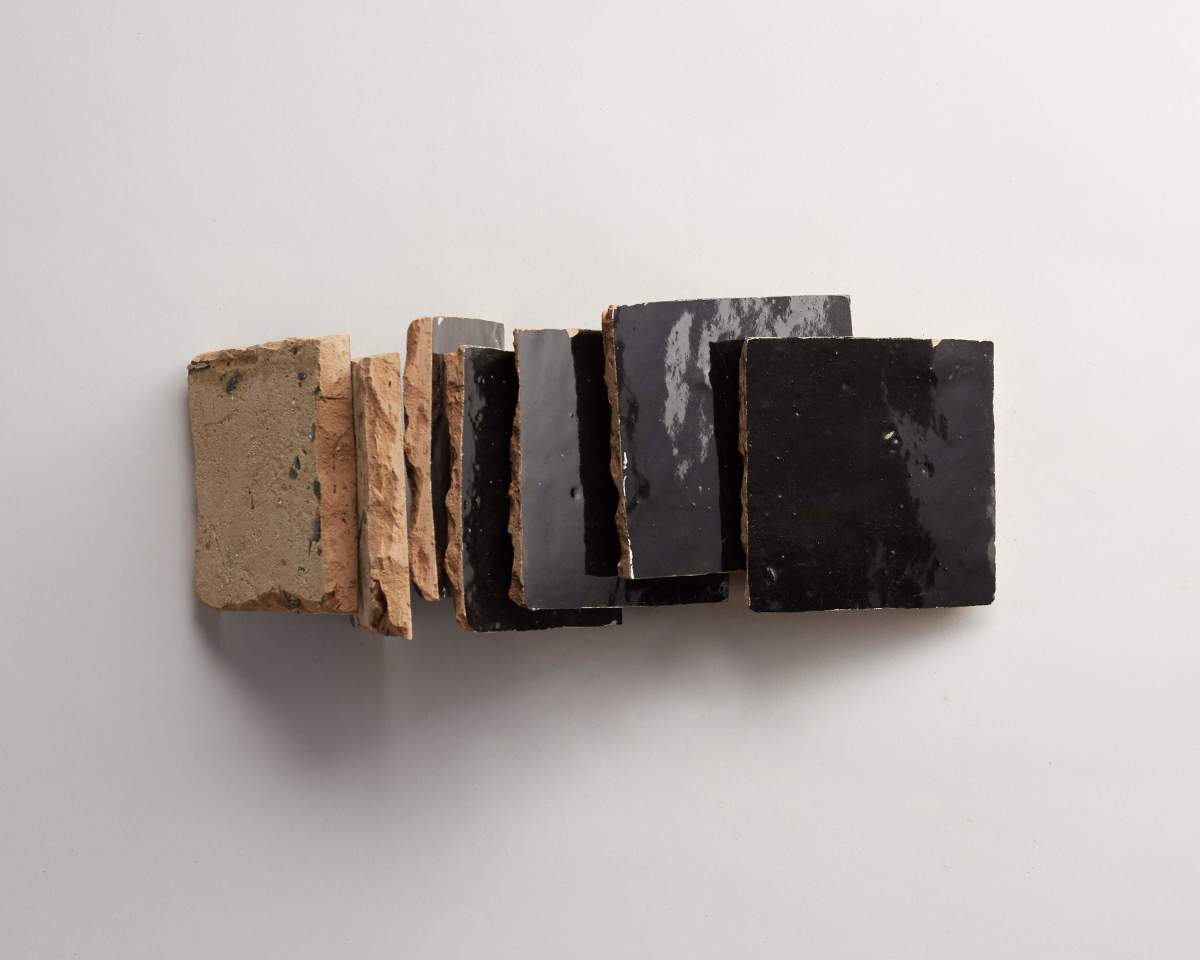 Seven rectangular, black-glazed ceramic tiles are aligned vertically on a white surface, showing both their glazed fronts and unglazed, rough backs.