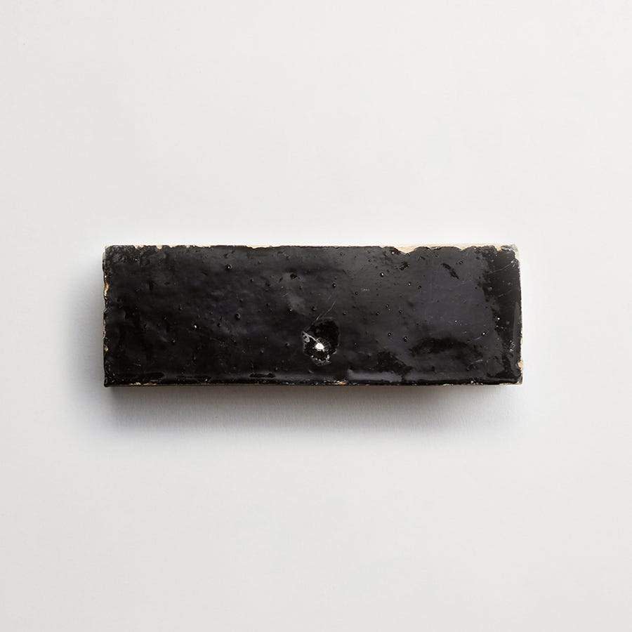 A rectangular piece of black licorice candy with a glossy surface on a plain white background.