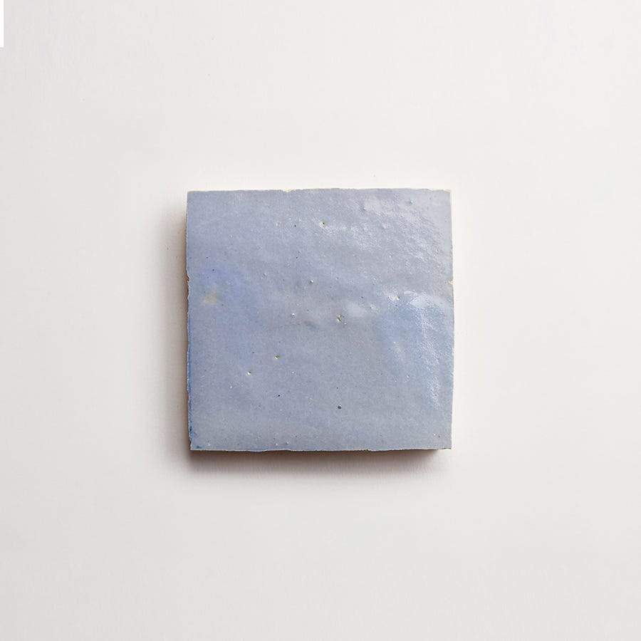 A single, square, light blue ceramic tile with a smooth, slightly glossy surface is centered on a plain white background.
