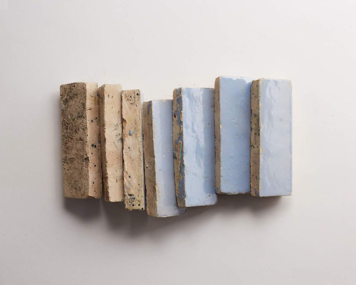 Seven rectangular ceramic tiles are arranged vertically on a white surface, with textures ranging from rough brown to smooth light blue.