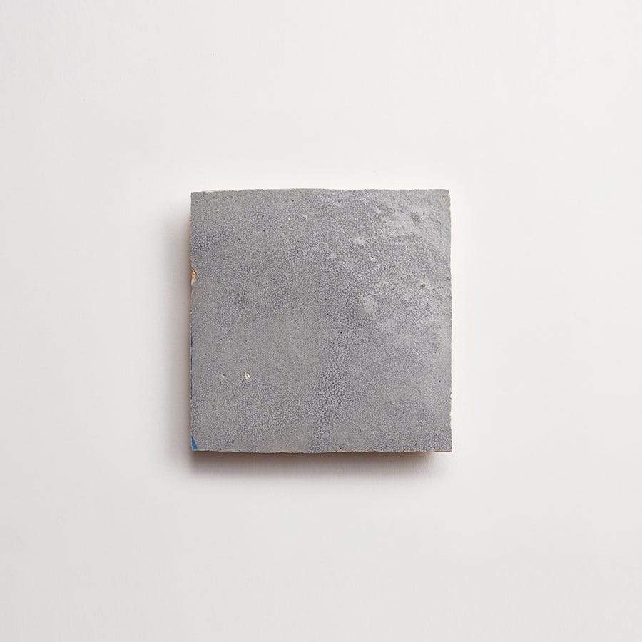 A single square gray tile with a rough, textured surface is centered on a plain white background.