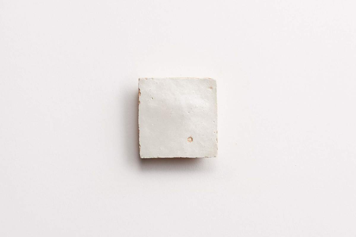 A small, square, white ceramic tile with a slightly rough texture and a small dot near the center, placed on a plain white background.