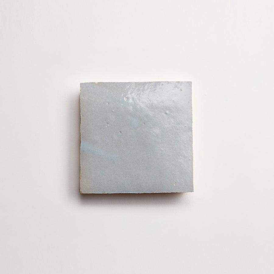 A single square, light gray ceramic tile with a smooth, slightly glossy surface is centered on a plain white background.