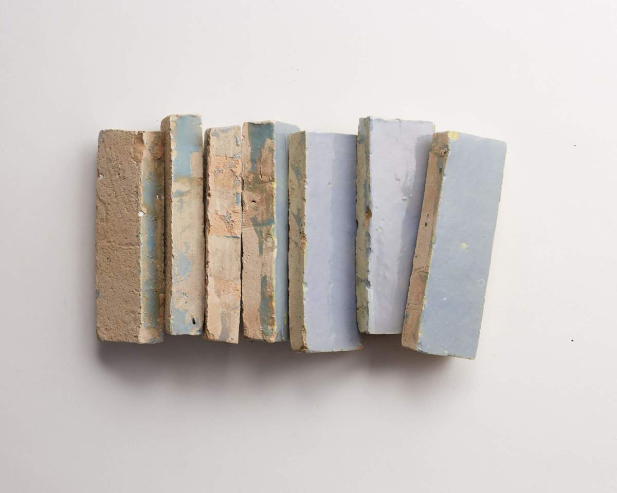 Seven rectangular bricks with rough surfaces in shades of beige and light blue are arranged vertically on a plain white background.
