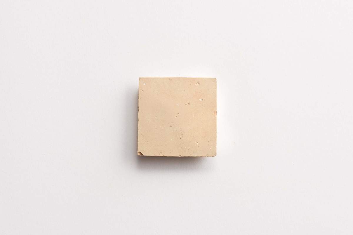 A square piece of beige clay or dough sits centered on a plain white surface.