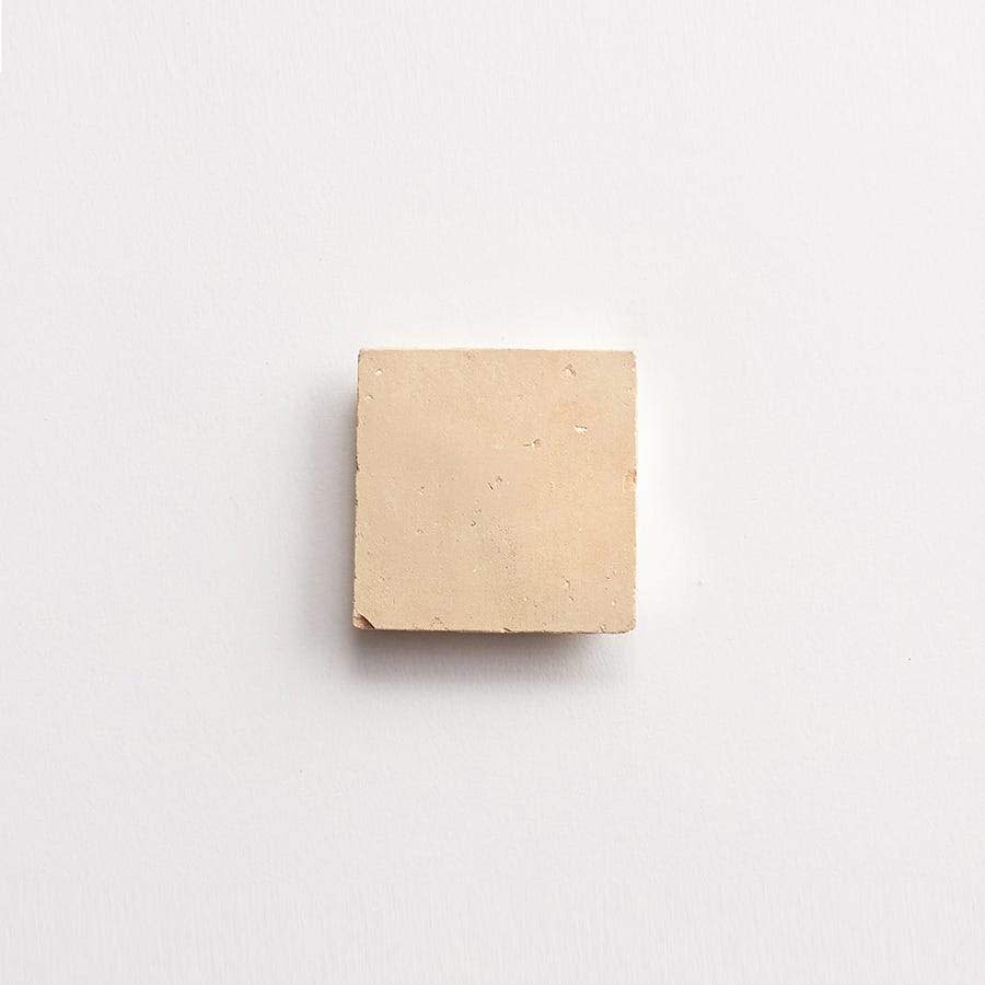 A small, square, beige tile is centered on a plain white background.