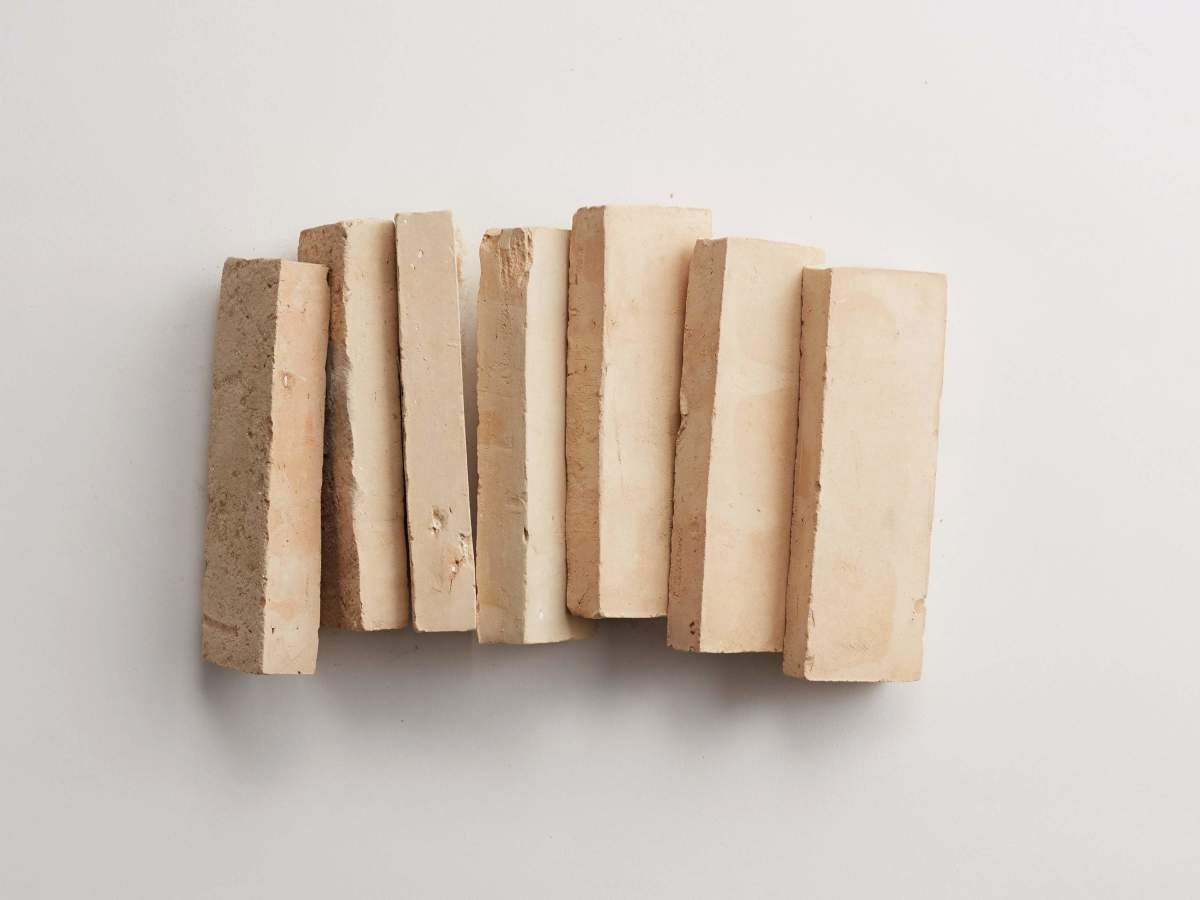 Seven beige rectangular clay bricks are arranged vertically in a slightly curved line on a plain white surface.