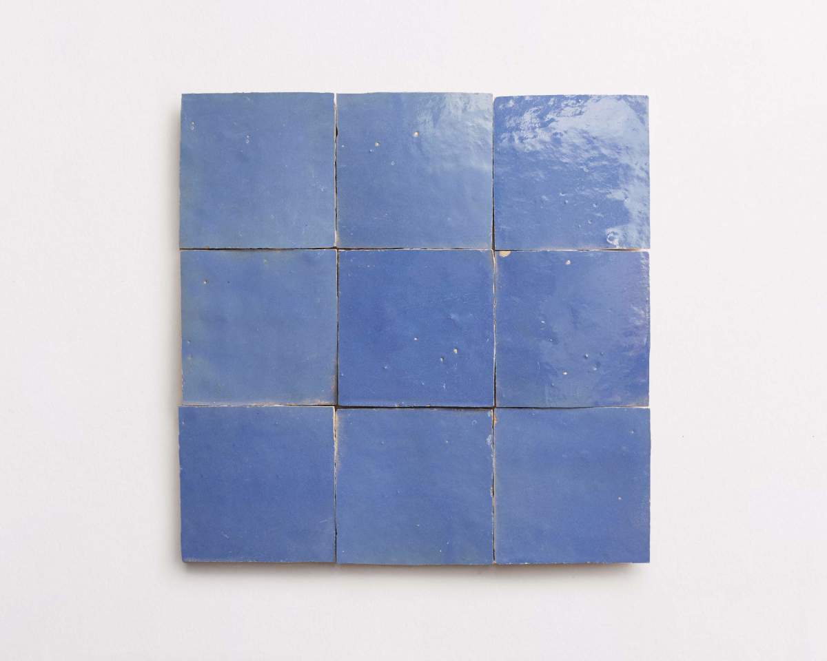 Nine blue ceramic tiles are arranged in a 3x3 grid on a white surface.