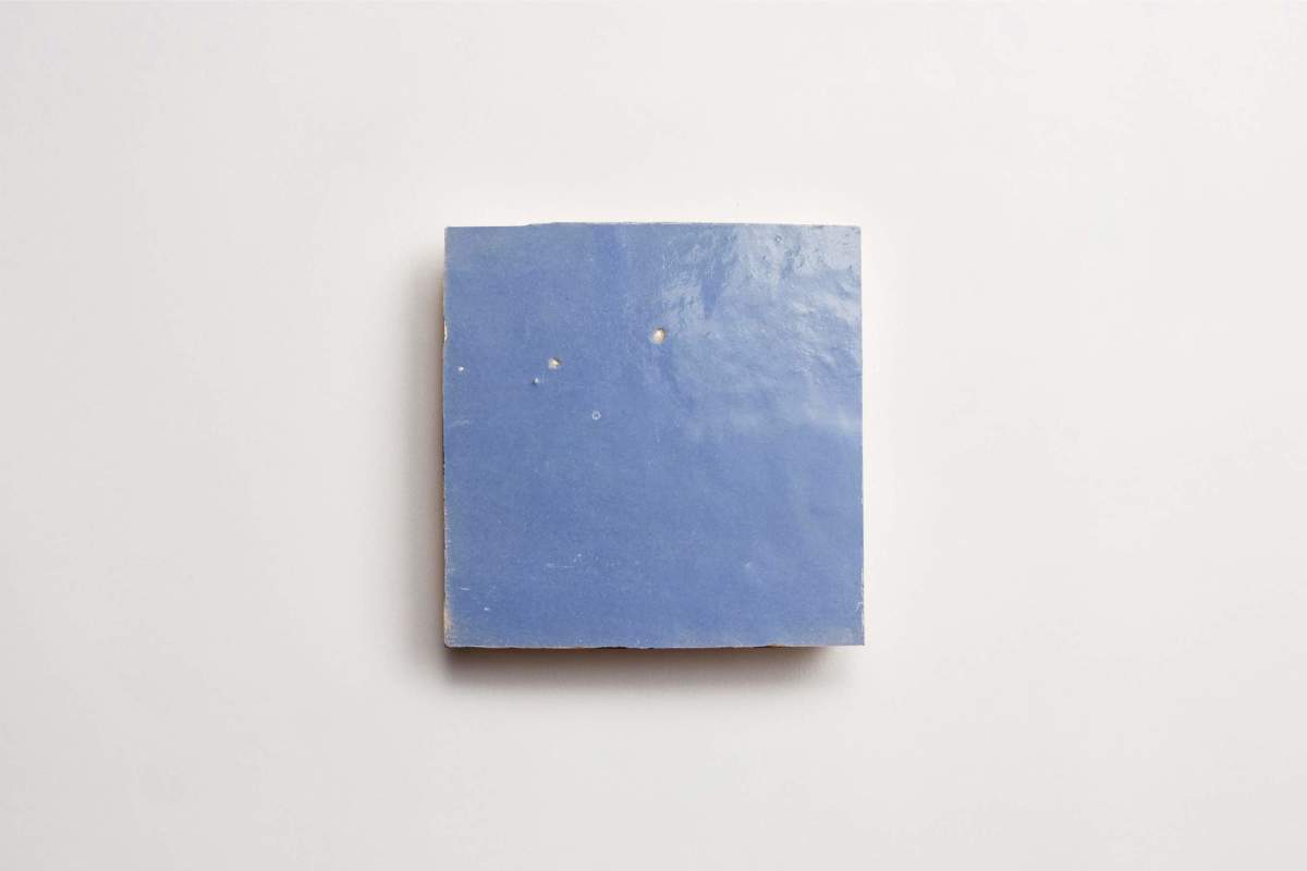 A single square blue ceramic tile with a glossy surface and minor imperfections, centered on a plain white background.