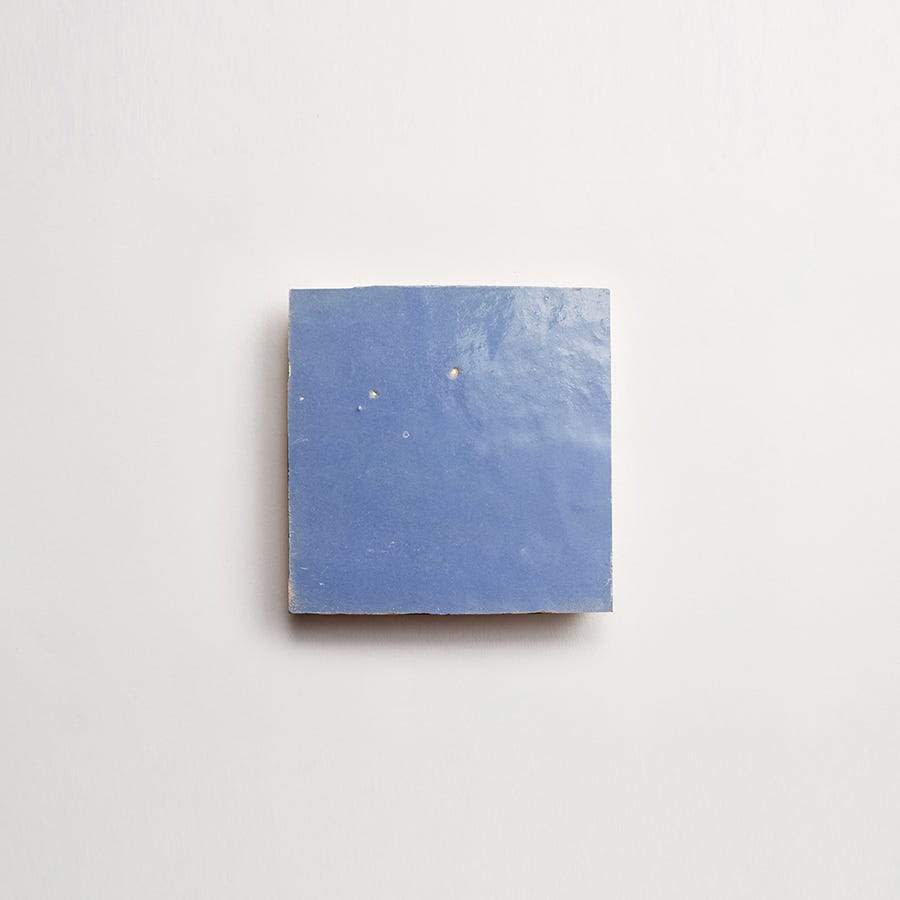 A single square blue ceramic tile with a glossy finish is centered on a plain white background.
