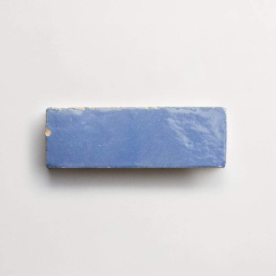 A rectangular, glossy blue tile with slightly chipped edges on a plain white background.