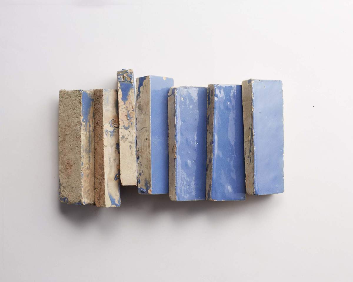 Seven rectangular bricks are arranged side by side on a white surface, with four painted blue and three showing a weathered, unpainted texture.