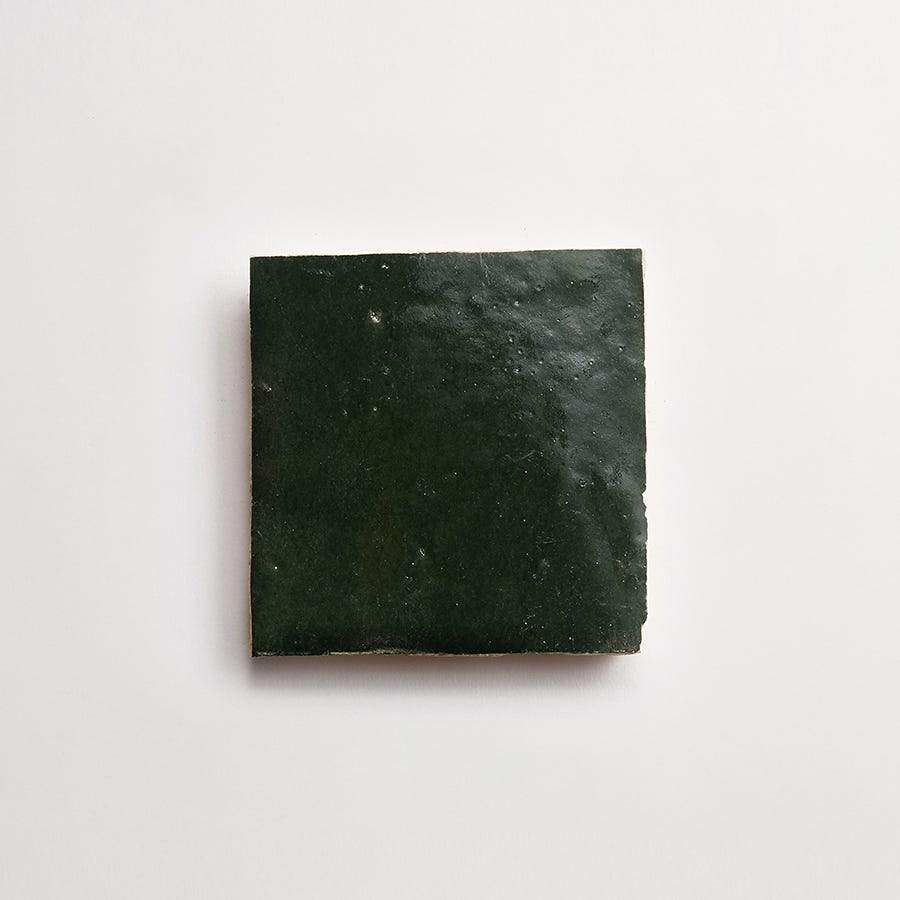 A single dark green square ceramic tile with a glossy finish, placed on a plain white background.