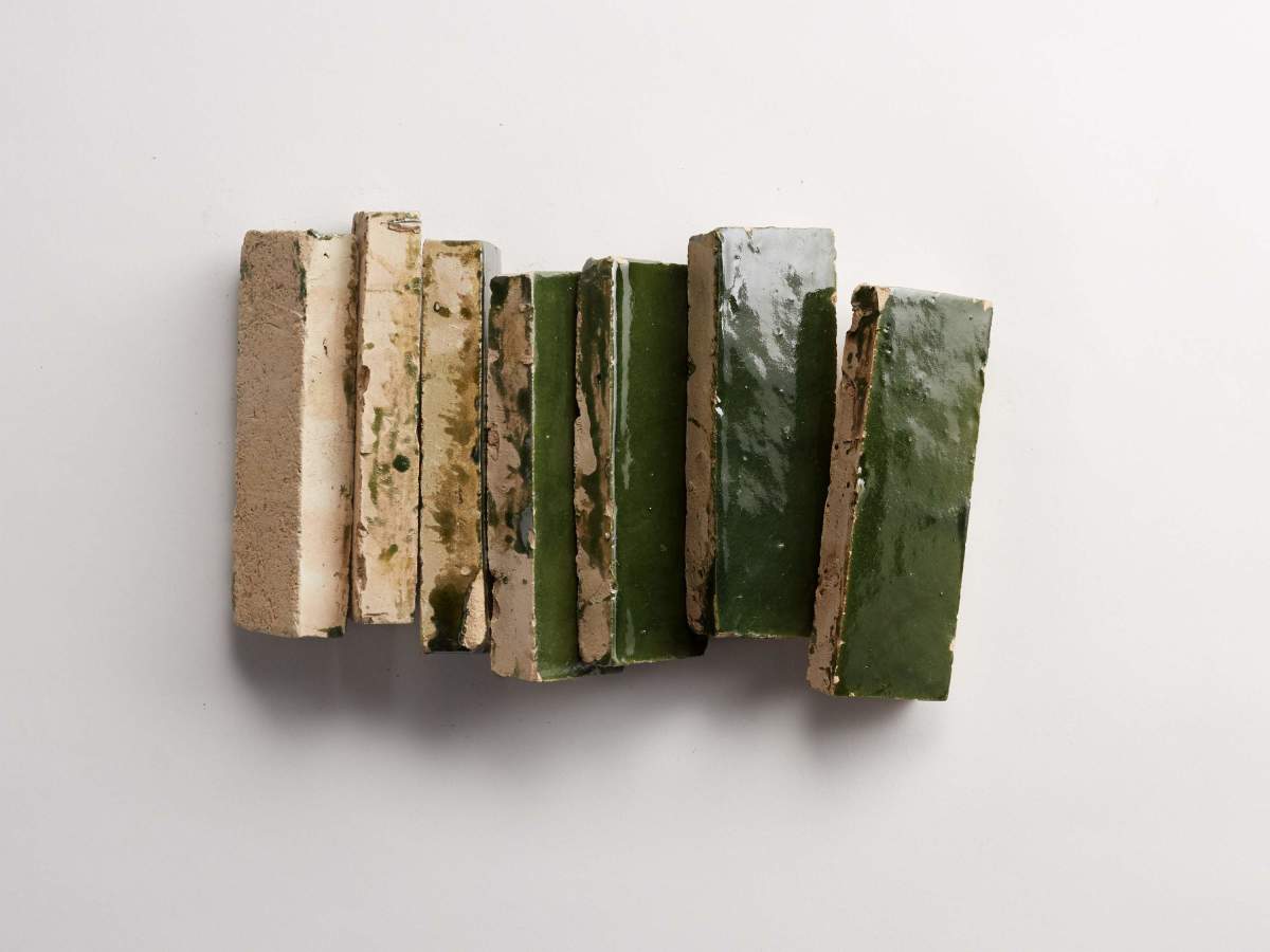 Seven rectangular ceramic tiles with green and beige glaze arranged side by side on a white surface.
